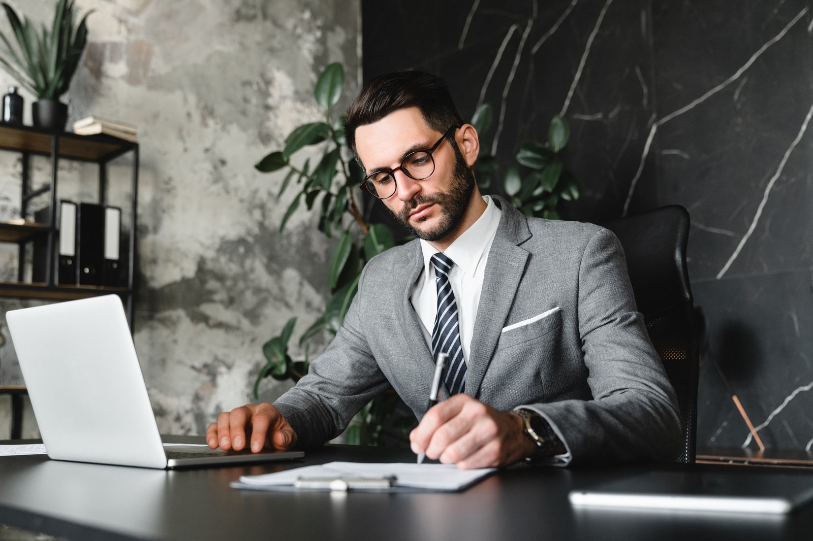 Smart young solicitor taking notes while using laptop for e-learning practice in office