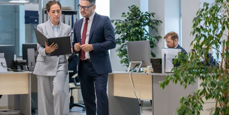 Two office workers in suit discussing contract terms while young woman holding folder