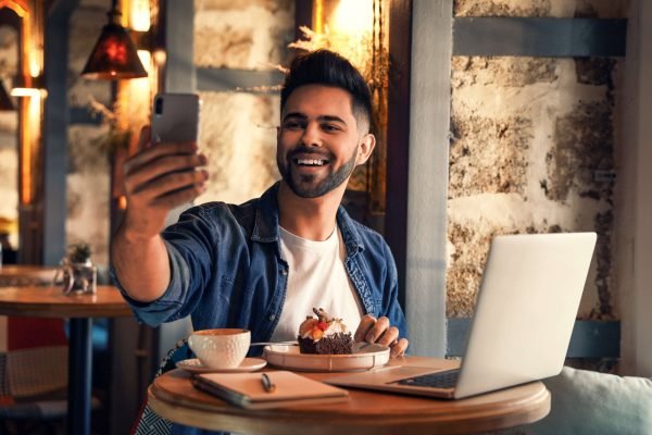 Young blogger taking selfie at table in cafe